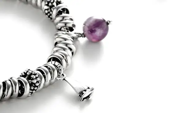 Pulsera de plata con charms, destacando una cuenta de amatista púrpura y un charm en forma de campana.