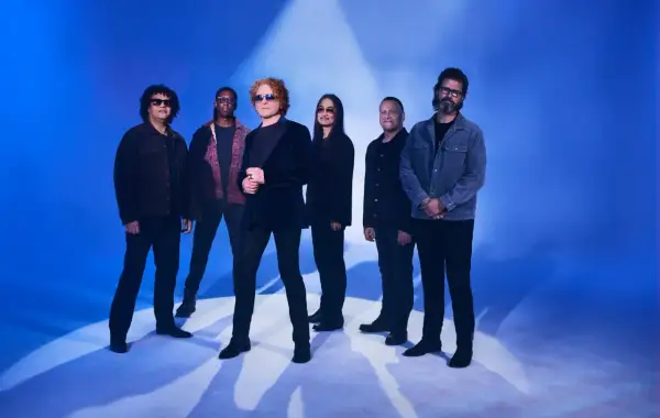 Zespół Simply Red gotowy na koncert. Muzycy pozują na tle niebieskiego światła, tworząc atmosferę nadchodzącego wydarzenia.