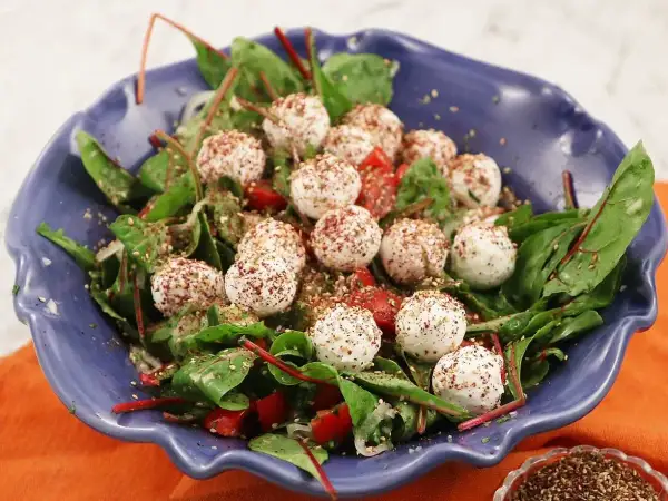 En blå skål med en sallad av gröna blad, körsbärstomater och små, kryddade labneh bollar.
