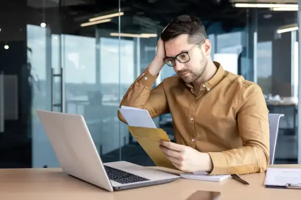 Uomo preoccupato legge una lettera di richiamo per ferie non concordate, con un laptop aperto davanti a sé.