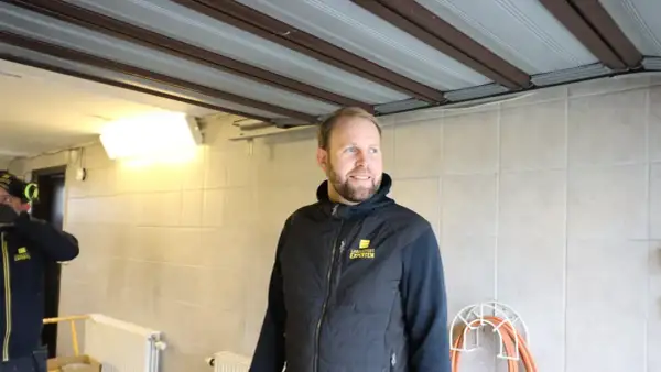 Man i väst med texten "Garageportexperten" ler. Ovanför syns en **täta garageport** i taket.