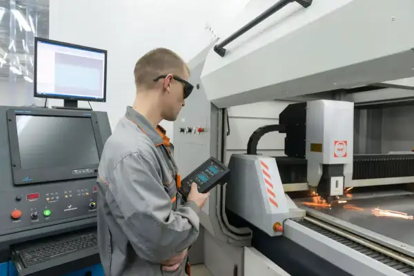 Operator w okularach ochronnych kontroluje proces programowania maszyn CNC za pomocą panelu sterowania.