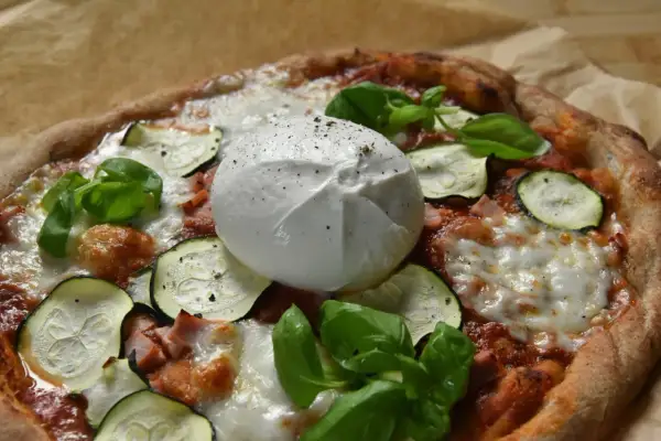 Pyszna pizza z burrata, cukinią i bazylią, posypana świeżo mielonym pieprzem.