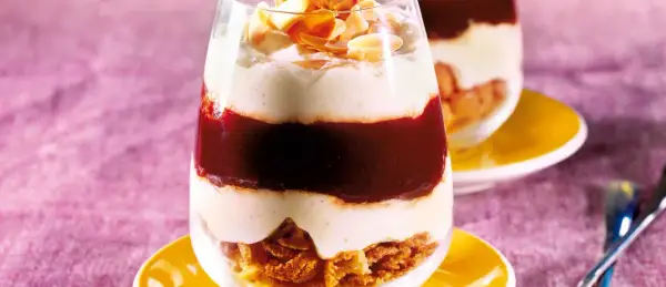 Schichtdessert im Glas mit zerbröselten Amarettini, roter Fruchtsauce und cremiger Masse, garniert mit Mandelblättchen.