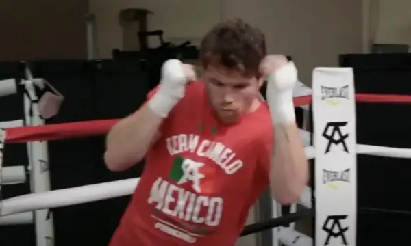 Boxer in a red "Team Canelo Mexico" shirt practices shadow boxing in a ring, his fists wrapped and ready.