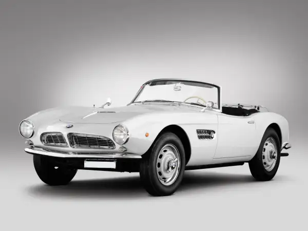 Biały kabriolet BMW 507 z lat 50. prezentuje się elegancko na szarym tle.