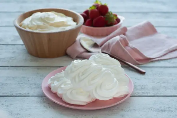 Creme double auf einem rosa Teller, daneben eine Schüssel mit Erdbeeren und ein Holzlöffel.