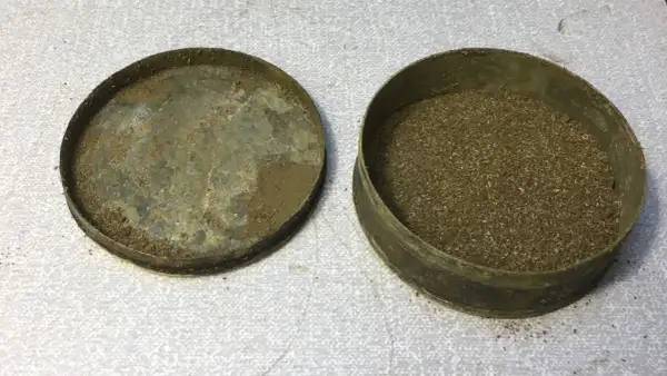 En gammal snusdosa med lock bredvid, fylld med utgånget snus.