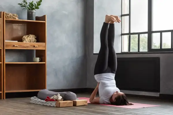 Frau praktiziert Iyengar Yoga in der Umkehrhaltung (Sarvangasana) auf einer rosa Matte, unterstützt von Holzblöcken.