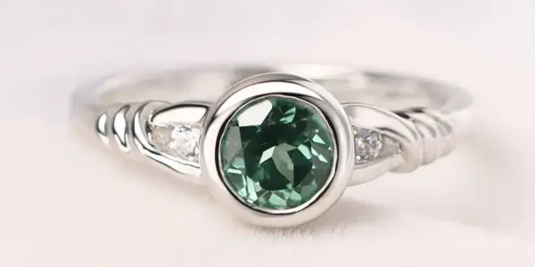 Anillo de plata con piedra verde ovalada y dos pequeños diamantes a cada lado, sujeto con un engaste bisel.