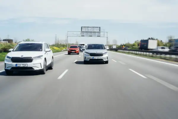 Na autostradzie biały i srebrny SUV jadą z zachowaniem bezpiecznej odległości między samochodami na światłach.