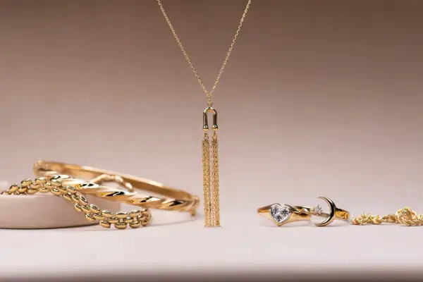 Elegantes conjuntos de oro para mujer: brazaletes, un collar con flecos dorados y anillos con forma de corazón y luna.