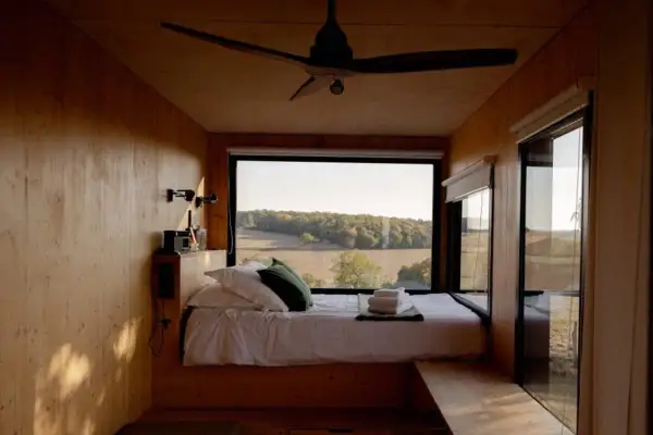 Intérieur d'une tiny house avec un lit douillet et une vue panoramique sur la campagne. Un endroit parfait pour se ressourcer.