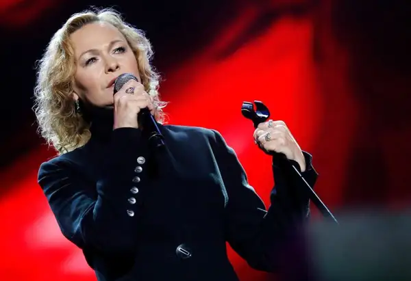 Artystka śpiewa z pasją, jakby mówiła "kocham cię życie tekst". Czerwone tło podkreśla jej emocje.
