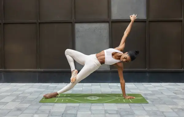 A woman in yoga attire performs a challenging pose on a mat, demonstrating how to block a hook with core strength and balance.