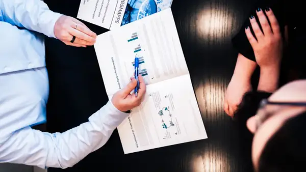 Zwei Personen besprechen ein Dokument über Private Equity und Rendite. Ein Mann zeigt mit einem Stift auf Diagramme.