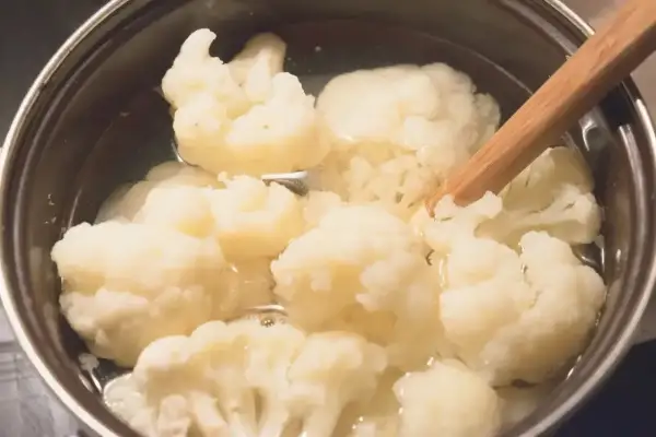 Gotowanie kalafiora w garnku. Drewniana łyżka miesza różyczki w gotującej się wodzie.