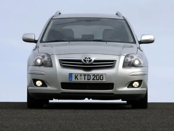 Srebrny Toyota Avensis z włączonymi światłami dziennymi i przeciwmgielnymi, gotowy do podróży.