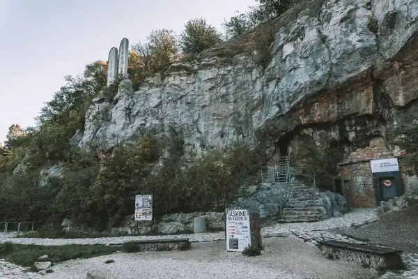 Kamieniste zbocze z wejściem do jaskini Kadzielnia. Schody prowadzą do ciemnego otworu, a obok tablice informacyjne.