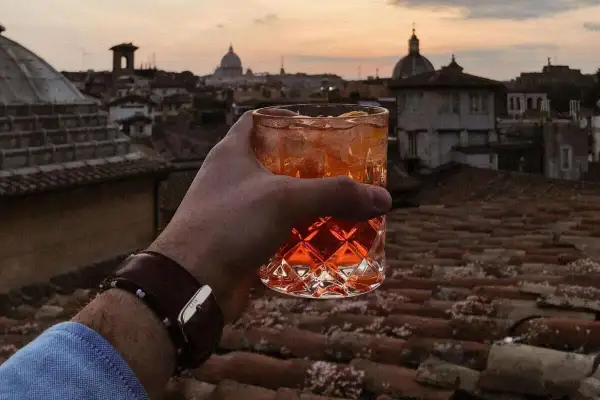 Un bicchiere di aperitivo con vista sui tetti di Roma centro al tramonto. Un momento perfetto per un apericena indimenticabile.
