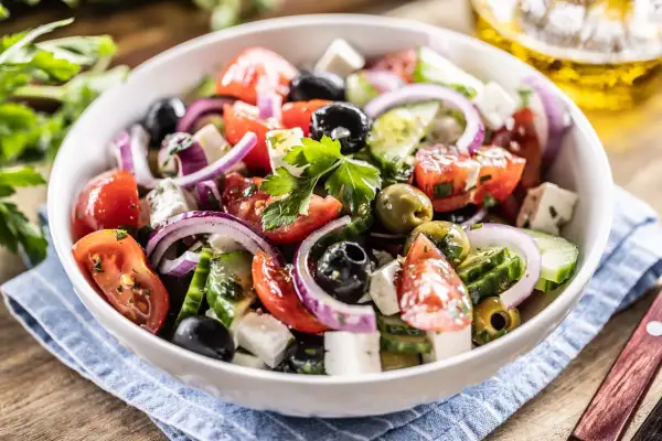Ensalada griega fresca con tomates, pepinos, aceitunas negras y verdes, cebolla morada y queso feta, adornada con perejil.