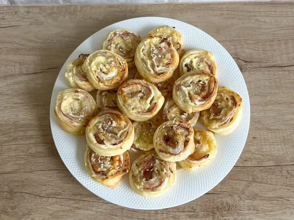 Talerz pełen chrupiących ślimaków z ciasta francuskiego z szynką i serem, posypanych sezamem. Idealna przekąska na imprezę.