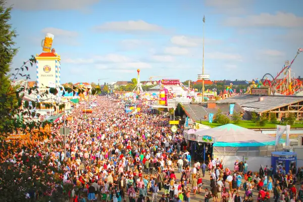 Folla immensa in **la città dell'Oktoberfest**, tra giostre, bancarelle e la torre Paulaner con un boccale di birra gigante.