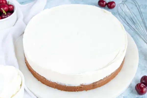 Ein runder Kuchen mit einer dicken Schicht luftiger **Mascarponecreme**. Kirschen und ein Schneebesen deuten auf die Zubereitung hin.