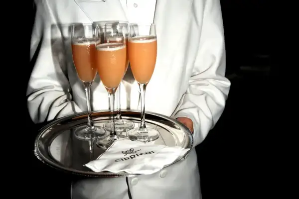 Kellner serviert Bellinis auf einem Silbertablett. So trinkt man Bellini: ein erfrischender Cocktail aus Prosecco und Pfirsichpüree.