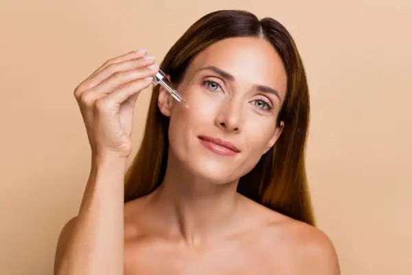 Donna applica un siero sul viso con un contagocce, un gesto essenziale per sapere come esfoliare la pelle e mantenerla luminosa.