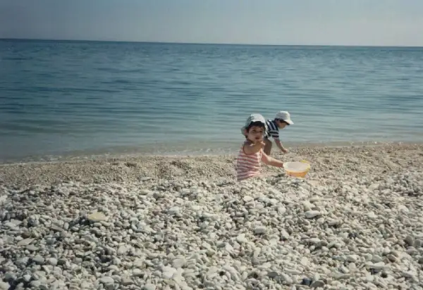 Bambini giocano sulla spiaggia di ciottoli a Marina di Montemarciano, con il mare azzurro sullo sfondo.