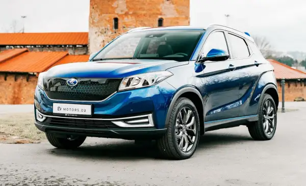 Błękitny SUV EV Motors.eu na tle ceglanych budowli. Jego nowoczesny design i ekologiczne serce przyciągają wzrok.