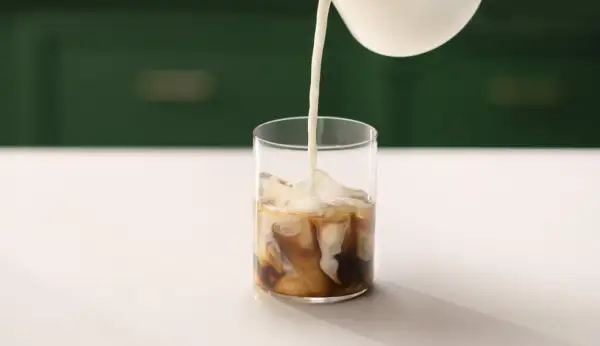 Mjölk hälls i ett glas med is och kaffe. Perfekt för ett enkelt iskaffe recept.