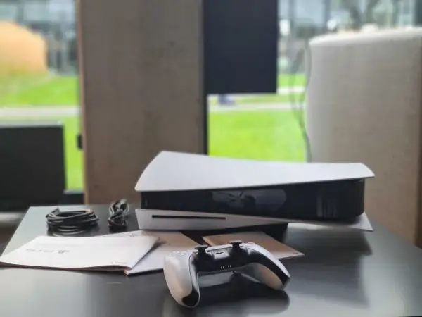Konsola PlayStation 5 z kontrolerem i kablami na czarnym stole.