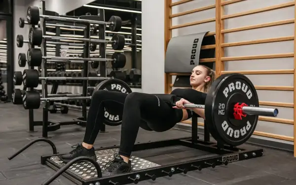 Kobieta wykonuje ćwiczenie hip thrust z obciążeniem na siłowni.