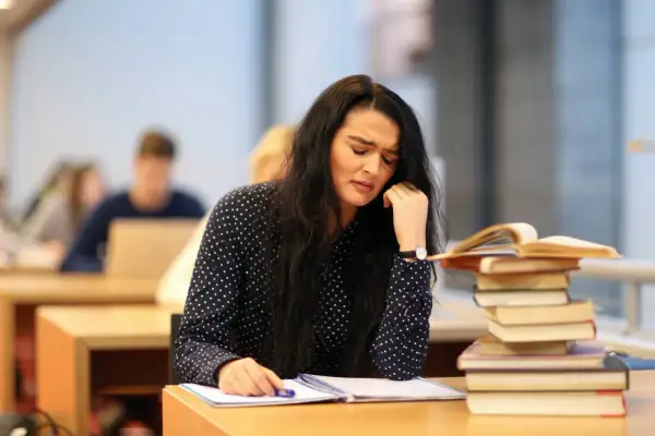 Verzweifelte Studentin mit Büchern. Sie überlegt, ob sie das **uni wechseln** soll.