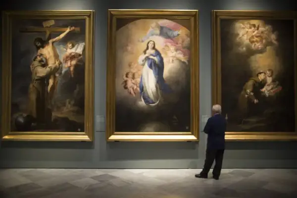 A man contemplates three religious paintings by Bartolomé Esteban Murillo in a gallery.