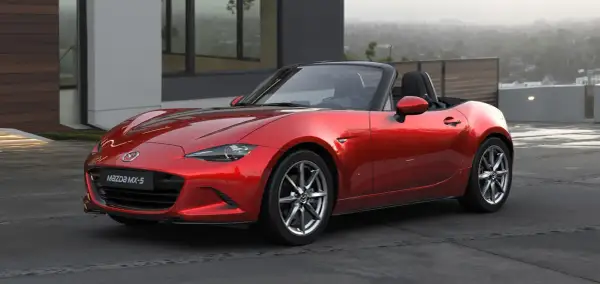 Czerwone Mazda MX-5, jedne z najbardziej pożądanych aut sportowych, lśni na tle nowoczesnej architektury.