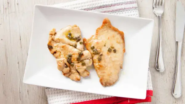 Due fette di fesa di tacchino con capperi su un piatto bianco. Un pasto leggero, ideale per chi cerca fesa di tacchino calorie.