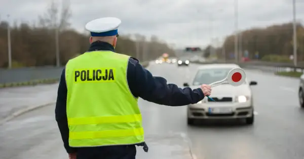 Policjant w kamizelce odblaskowej zatrzymuje samochód. Kierowca rozmawiający przez telefon może spodziewać się mandatu.