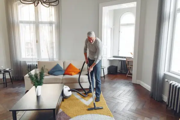 Mężczyzna odkurza dywan w salonie. Sprzątanie w domu to jego sposób na relaks.