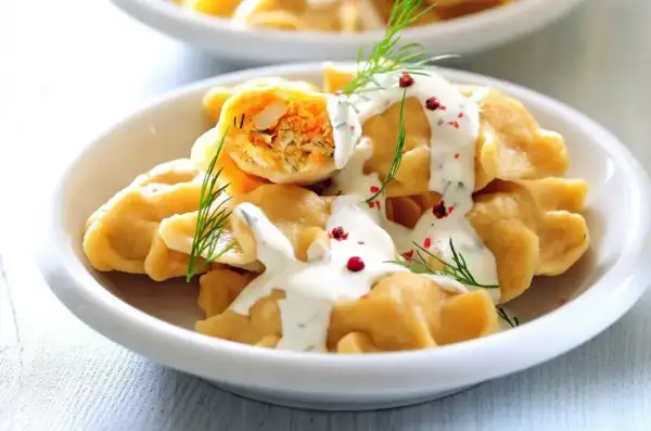 Pierogi z farszem, polane sosem, udekorowane koperkiem i pieprzem.