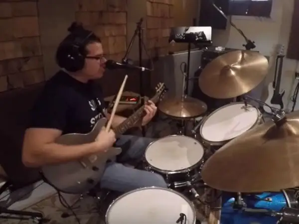 Muzyk w słuchawkach gra na gitarze i perkusji, jakby wpadł w **rush tom sawyer**.
