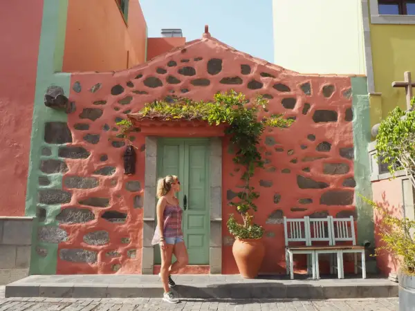 Una mujer posa frente a una casa de piedra y coral con puerta verde en Gran Canaria.