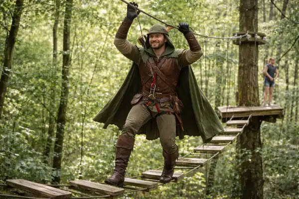 Un homme en costume de Robin des Bois traverse un pont suspendu dans un parc d'accrobranche, une aventure à Paris.