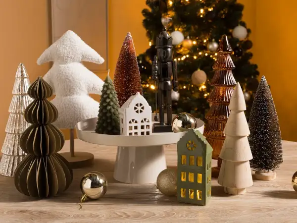 Kerstboom decoratie in Scandinavische stijl: diverse kerstboompjes, een notenkraker en huisjes op een houten tafel.