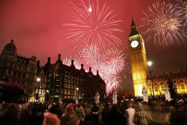 Fuegos artificiales iluminan el cielo sobre el Big Ben y el Parlamento, celebrando las festividades inglesas con una multitud expectante.