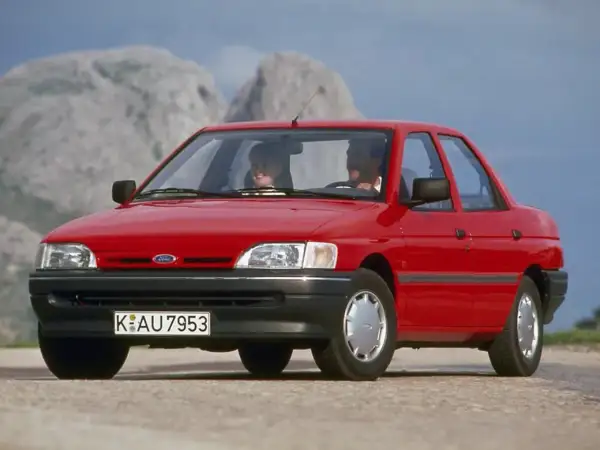 Czerwony Ford Orion z parą uśmiechniętych ludzi w środku, jadący po górskiej drodze.