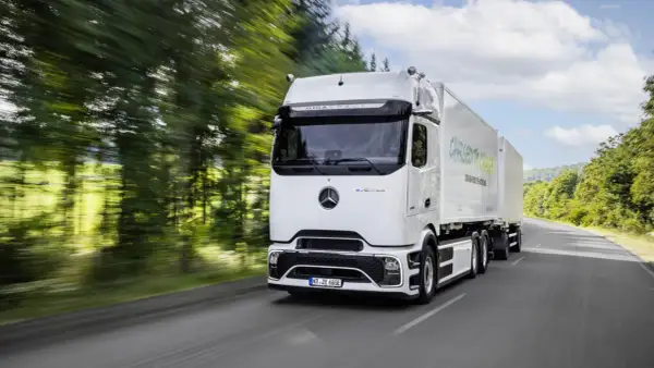 Un camion électrique Mercedes eActros GigaSpace roule sur une route bordée d'arbres.