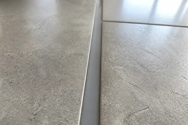 Gros plan sur un joint de dilatation carrelage gris, entre deux carreaux texturés.